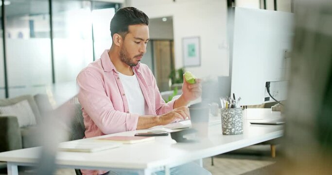 Asian man, working and eat apple in office for lunch time snack, planning tech strategy on pc and checking phone. Businessman, smartphone and typing on computer with healthy food for diet nutrition