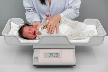 crying newborn baby weight measurement on digital scales with doctor in hospital