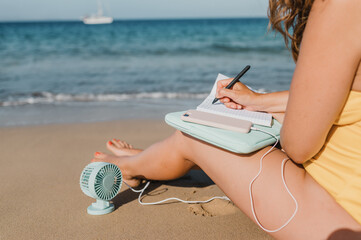 Unrecognizable woman writing on notebook near sea