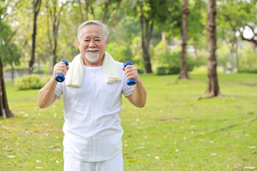 Happy and smiling asian senior man doing arm work out and lifting dumbbell exercise with relaxation for healthy in park outdoor after retirement. Health care elderly outdoor lifestyle concept.