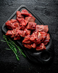Sliced raw beef on a black cutting Board with rosemary.