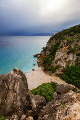 Fototapeta na wymiar Sandy Beach on a rocky coast near Cala Gonone, Sardinia. Cloudy Sunrise Sky.