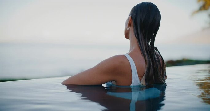 Beautiful young woman relaxing in luxury infinity pool on vacation at tropical resort spa