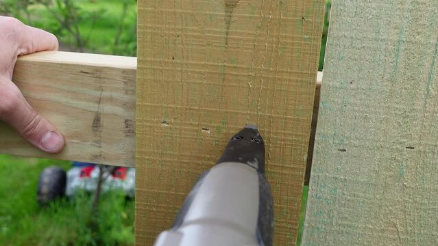 Hands of person use pneumatic nail gun for wooden fence, close up