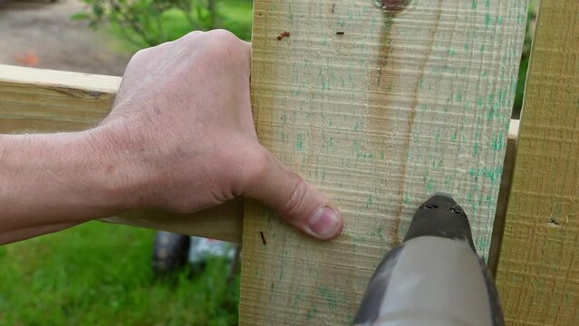 Man using pneumatic nail gun on wooden fence, close up view
