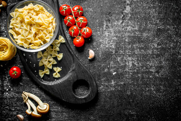 Raw farfalle and tagliatelle paste in a bowl on a cutting Board with mushrooms, tomatoes and spices.