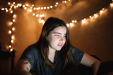 Happy young female teenage student looking at laptop computer screen while studying at home at night