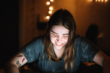 Happy young woman smiling looking at laptop computer screen at home at night