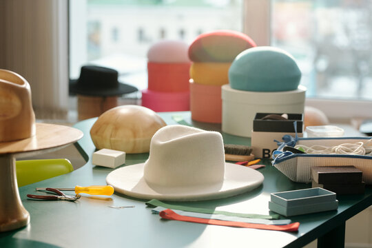 White felt hat, group of berets and wooden workpieces on workplace of modern fashion designer and owner of craft shop selling trendy apparel