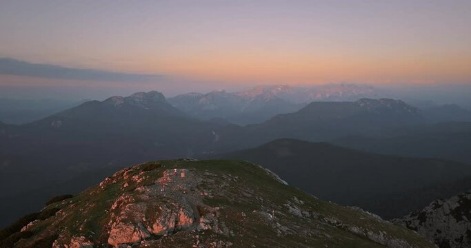 A drone shot of the top of mountain Peca in the early morning, Light orange colors in the sky, one hiker standing at the top.