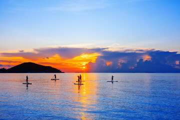 People silhouettes stand SUP paddle boarding, sea sunset beach, active young man woman surfing...