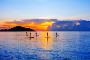 People silhouettes stand SUP paddle boarding, sea sunset beach, active young man woman surfing paddling board, ocean sunrise, surfboard, healthy lifestyle, water sport, summer holidays, relax vacation - obrazy, fototapety, plakaty