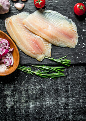 Fish fillet with chopped onion in bowl, garlic and rosemary.