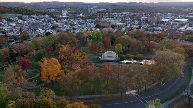 Aerial orbit following bend in road through city park. Reading Pennsylvania drone footage during autumn, Colorful leaves and foliage.
