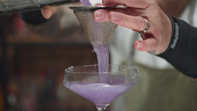 Close-up of pouring the finished cocktail from a shaker into a glass. The bartender prepares alcoholic cocktails for a fiery party at the bar. High quality 4k footage