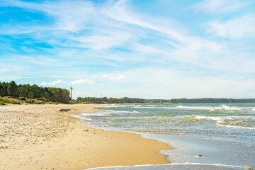 A sandy seashore with green bushes along the edge. Background with a summer view of the sandy beach.