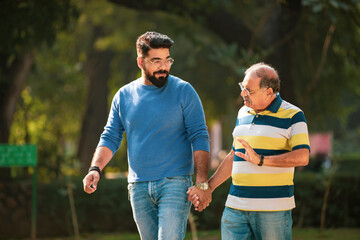 Old indian father talking with his young son at park.