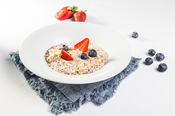 Oatmeal with almonds, blueberries and strawberries in a white plate on a white background