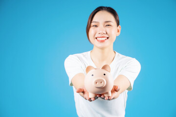 Fototapeta na wymiar Photo of young Asian woman holding piggy bank on background