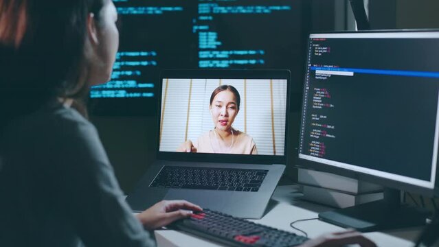 Asian woman developer programmer, software engineer, IT technical support center talking with team via video call. Working on computer overtime to check coding in bugging system