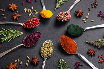 Variation of spices in metal spoons paprika, turmeric, cardamom, a mixture of allspice, thyme and...