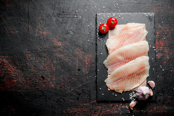 Fish fillet on paper on a stone Board with garlic and tomatoes.