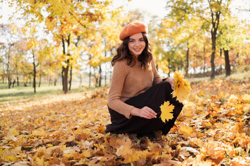 Happy smiling young woman in park on sunny autumn day collections leaves. Cheerful female in...