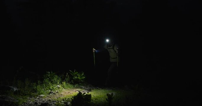 Hiker walking up a mountain in pith black just before the dawn, illuminating his path with a headtorch.
