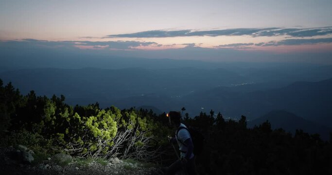 Hiker walking past the camera with the hiking polesa and headtorch looking at hte valley and direction of where the sun will rise.