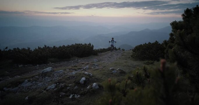 Hiker walking on a rocky path with hiking poles in early morning before the sunrise.
