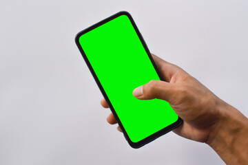 Mock up mobile. Man's hand holding black smartphone with green screen in vertical position isolated on white background.