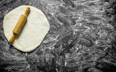 Dough for cooking homemade pizza with a rolling pin.