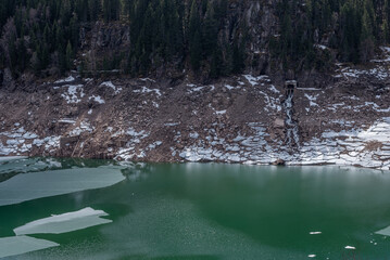 Water flowing into the river, snow lie on the stones on the bank of the river, panorama.	