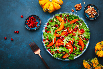 Healthy eating pumpkin salad with baked sweet pumpkin, lettuce, arugula, pomegranate seeds and nuts. Comfort food. Blue background. Top view