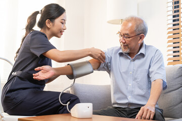 Pressure measurement of hypertension in elderly man sitting on couch, young woman nurse or...