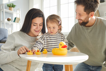 Family and parenthood. Baby girl and her caring young mom and dad are playing with rubber toy ducks...