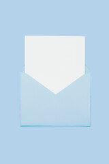 Closeup on blank empty white paper card in blue opened envelope isolated on blue pastel color background. Love letter minimal concept. Conceptual layout template with text place on postcard. Mock-up 