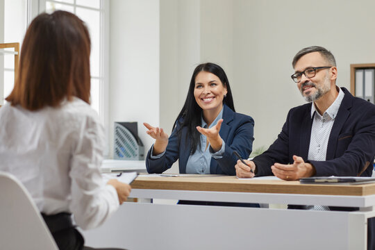 Smiling, friendly businessman with his beautiful colleague conducts interview for young girl for further cooperation and productive work in team. Positive atmosphere in spacious modern office.
