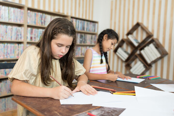 Two girl using colour pencil drawing on paper in the classroom at school. Group of girl studying art in the classroom. Children and education concept