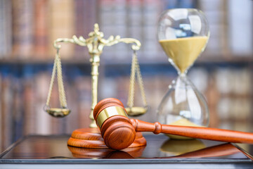 Legal office of lawyers, justice and law concept : Judge's gavel or hammer and base used by a judge person on a desk in a courtroom with blurred weight scale of justice, bookshelf, hourglass behind.