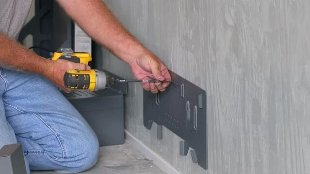 Technician using a drill to install the hanging bracket for the battery box supports; concepts of home backup power, solar power, alternative energy, and sustainability