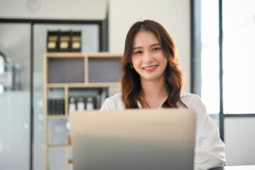 Beautiful Asian businesswoman using laptop computer, smiling and looking at the camera.