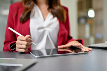 A female office worker using her digital tablet with stylus pen at her desk. cropped image