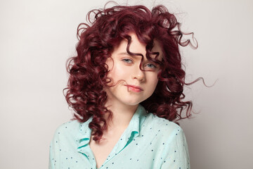 Happy woman in blue shirt with red curly hair on white wall background