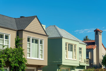 Row of residential houses in suburban neighborhood with front yard trees and blue sky with visible windows and roofs