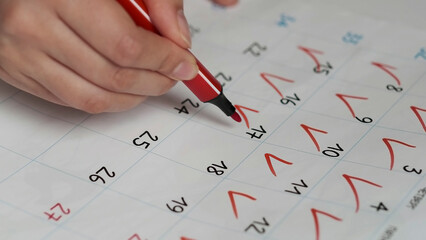 Blurred calendar page. Close-up female hand cross out days in calendar. Red circle marked with pen on a calendar sheet