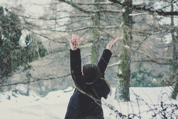 Fototapeta na wymiar Enjoying first snow in forest scenic photography. Picture of woman raising arms up with snowy woodland on background. High quality wallpaper. Photo concept for ads, travel blog, magazine, article