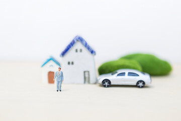 Miniature business man over blurred house and car model on white background, property and asset investment, successful life style