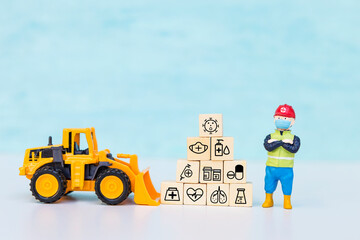 Miniature worker wearing safety helpmets with medical icon cube and yellow front loader truck with space on blue background, health and medical concept