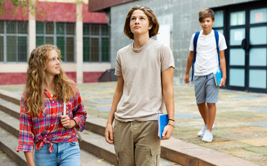 Teenagers boy and girl going home after school. Younger boy walking behind them.